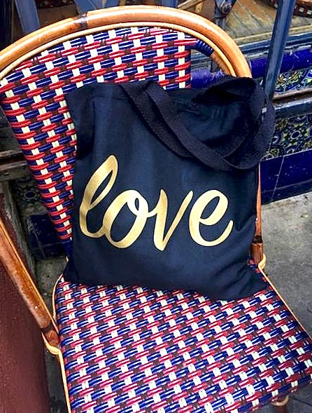 We Love this tote! Cotton canvas fabric tote in black with 'LOVE' screen printed in gold in cursive style. The perfect size to take wherever your heart's desire. Dimensions: 14" x 14" Machine wash, cold. Line Dry. Made in California