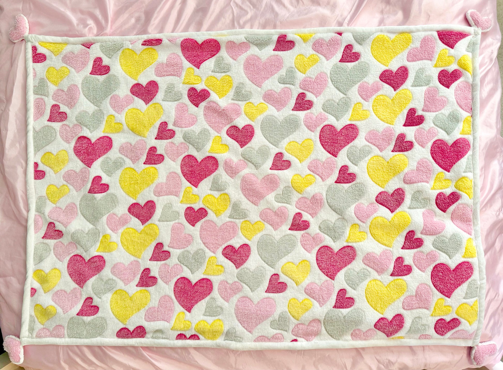 Cuddly soft, plush fabric blanket with multi-colored hearts in light & dark pink, yellow and light gray, in different sizes on one side, and solid white on the reverse side. Special detailing with puffy hearts on each corner of the blanket. Dimensions: 48" long x 36" wide Delicate wash cold, dry low heat Made in the USA