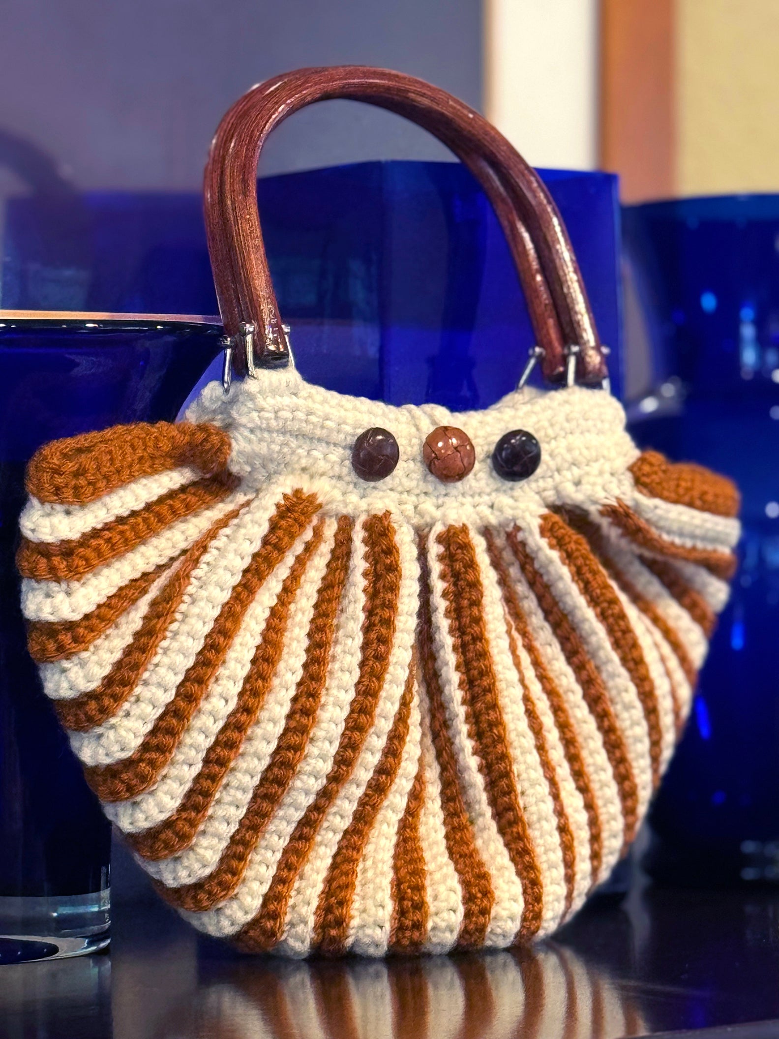 Venetian style, one-of-a-kind vintage crocheted bag by Oda G. Handcrafted with upcycled acrylic yarn in cream & cinnamon stripe pattern, vintage wood handles and buttons (on both sides) in complimenting brown tones. Dimensions: Length: 12"(longest part) Height: 9" (with 5"handles 14") Width: 4" Handwash cold, Dry flat, or Dry Clean Made in the USA